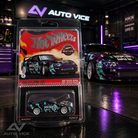 A Hot Wheels diecast model car in its original blister packaging, displayed in the foreground with a real purple Toyota Supra race car in a garage setting in the background.