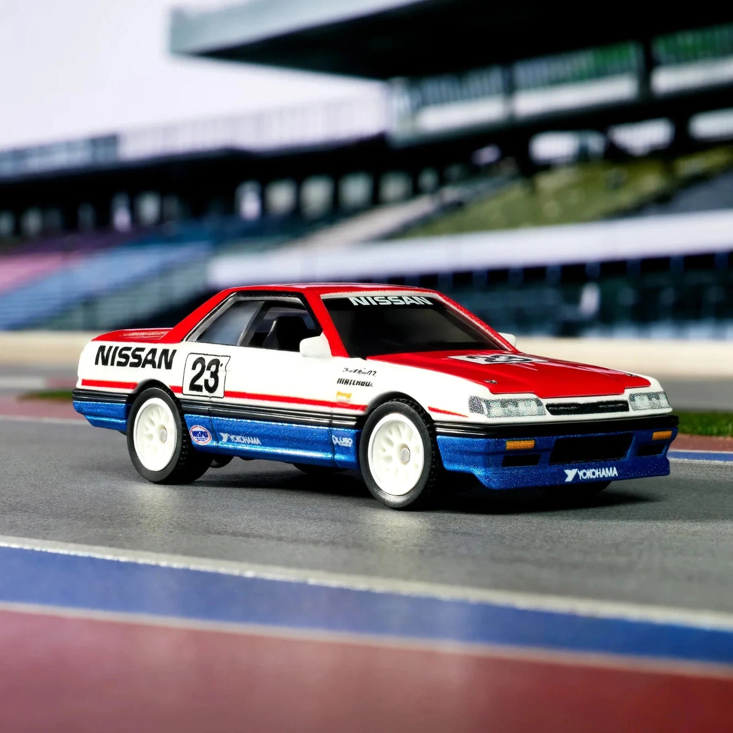 A diecast model of a classic Nissan Sylphy race car, number 23, featuring a red, white, and blue livery with decals, displayed on a miniature racetrack.