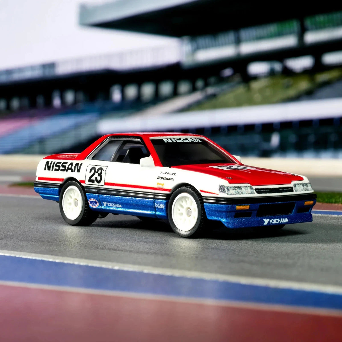 A diecast model of a classic Nissan Sylphy race car, number 23, featuring a red, white, and blue livery with decals, displayed on a miniature racetrack.