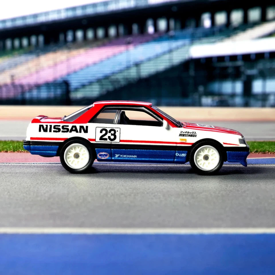 A diecast model of a Nissan Escort RS Cosworth race car, number 23, featuring a white, red, and blue livery with sponsor decals, displayed on a racetrack surface with blurred grandstands in the background.